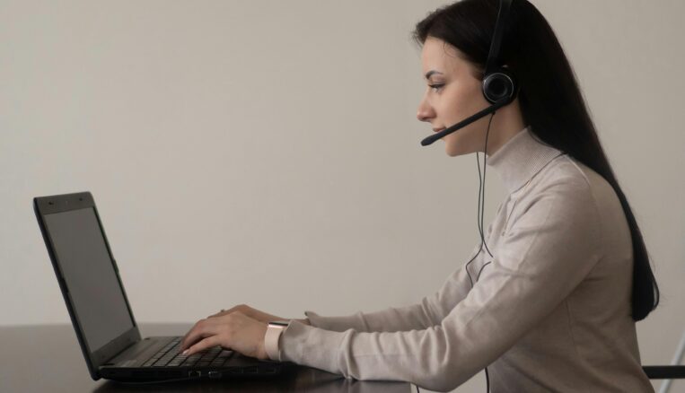 Young woman with a grey jumper in a professional workspace using a laptop with a headset
